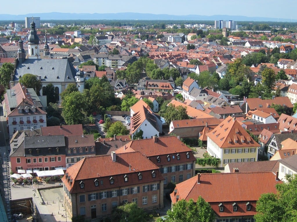 Luftaufnahme einer europäischen Stadt mit Gebäuden mit roten Dächern, Bäumen und einem Kirchturm.