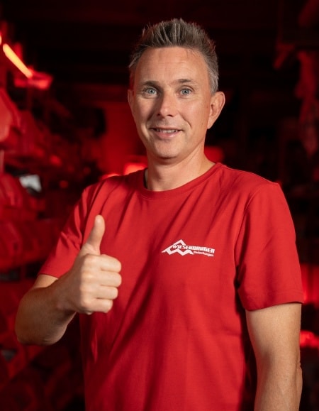 Mann im roten T-Shirt, der lächelnd den Daumen nach oben streckt, mit dunkelrotem Hintergrund.